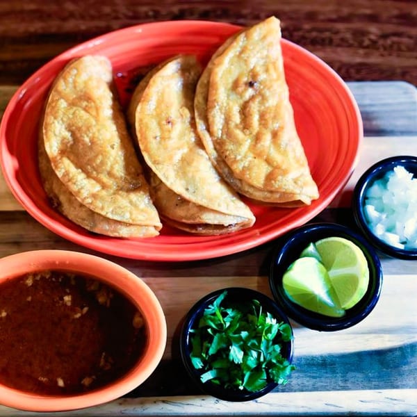 Three golden-brown La Patrona Cantina and Grill empanadas on a red plate with sides of salsa, cilantro, lime, and onions.